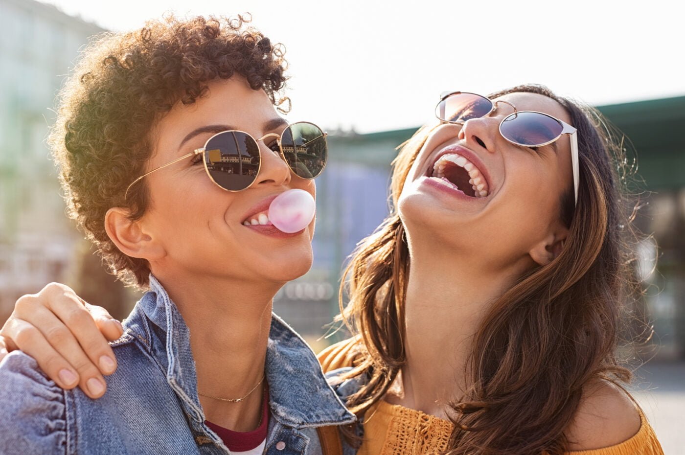 Young latin woman laughing while friend inflating bubble gum._Meeting Point Health