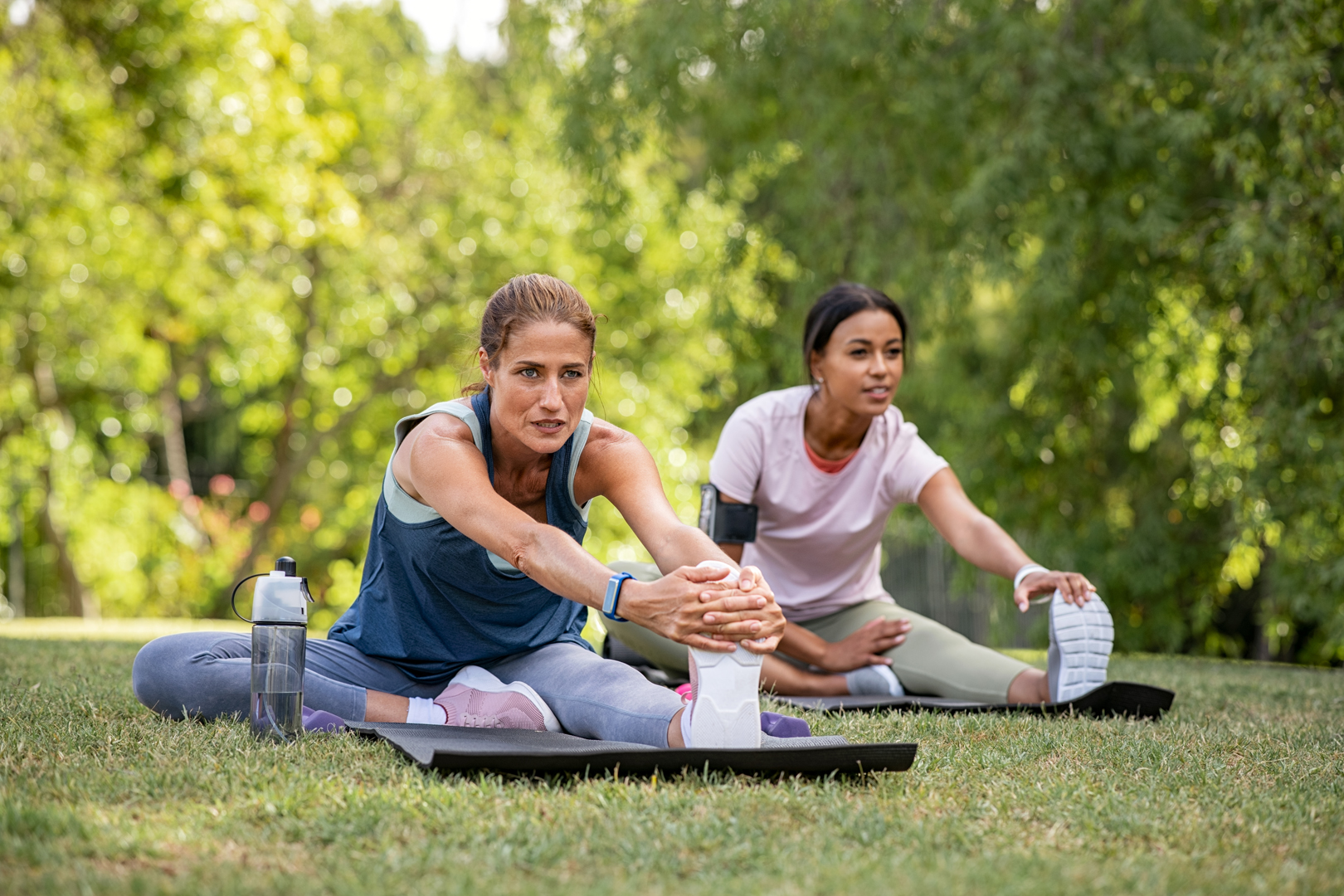 Two mature woman stretching their legs after exercise in park.