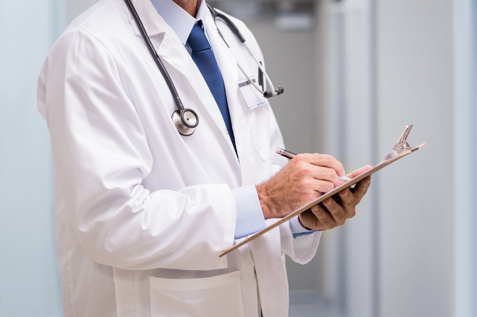 Close up of hands of senior doctor writing on a clipboard at hospital.