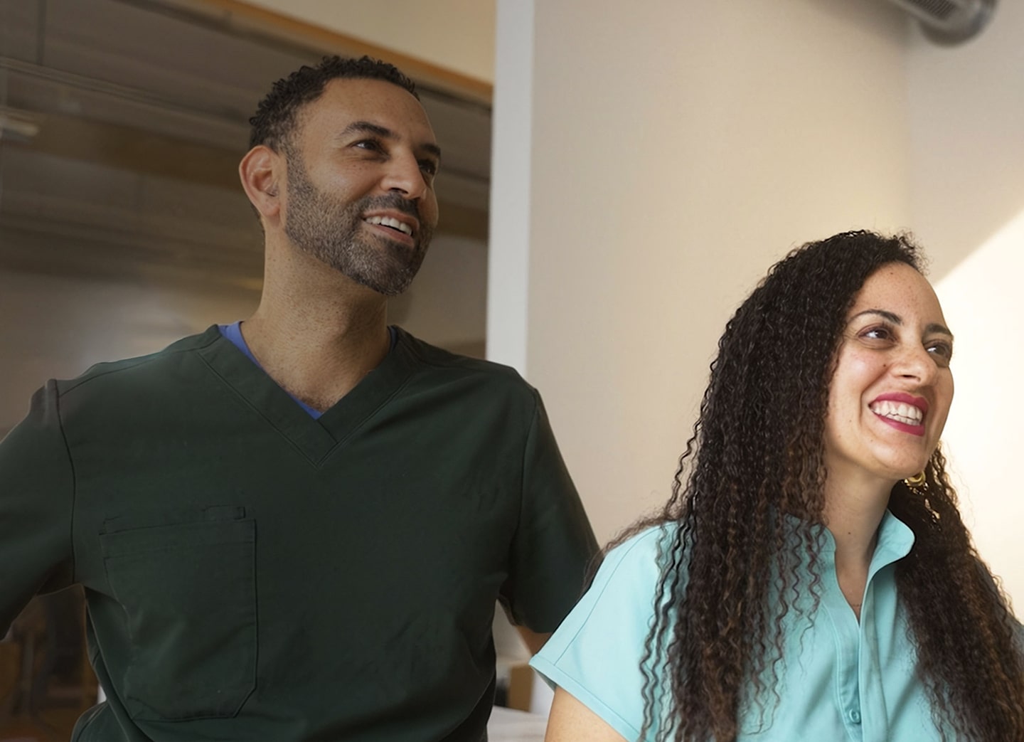 Dr. Stephen and Mary Anne Matta wearing scrub stand in a brightly lit hallway, appearing professional and ready for work.