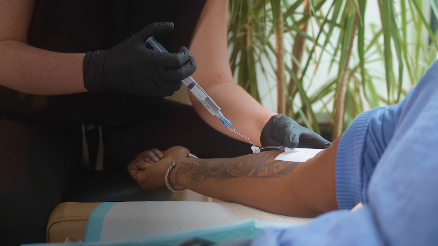 A person sitting in a chair receiving IV therapy, with medical equipment visible nearby.