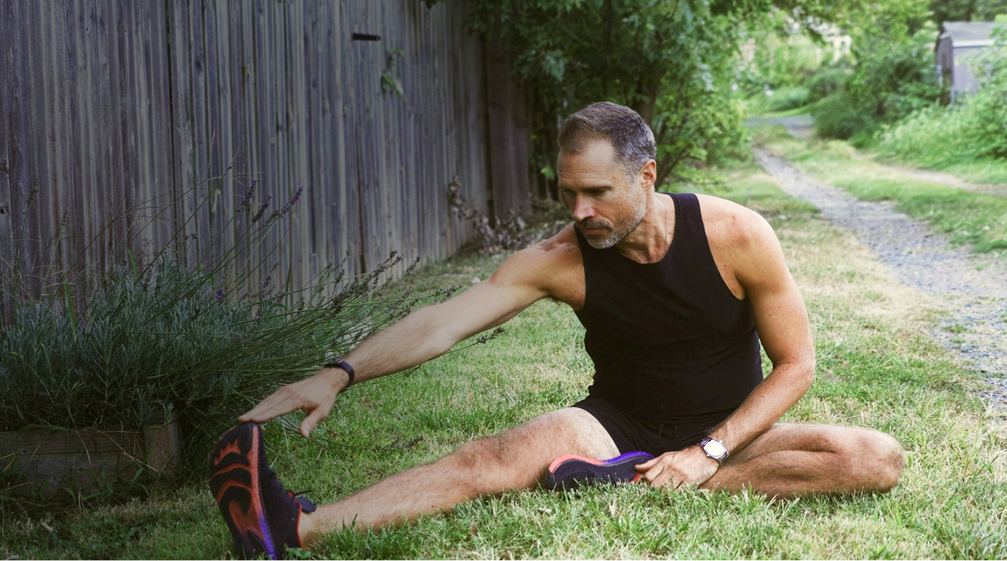 A man stretches his legs on the grass, embodying vitality and an active lifestyle in a serene outdoor setting.