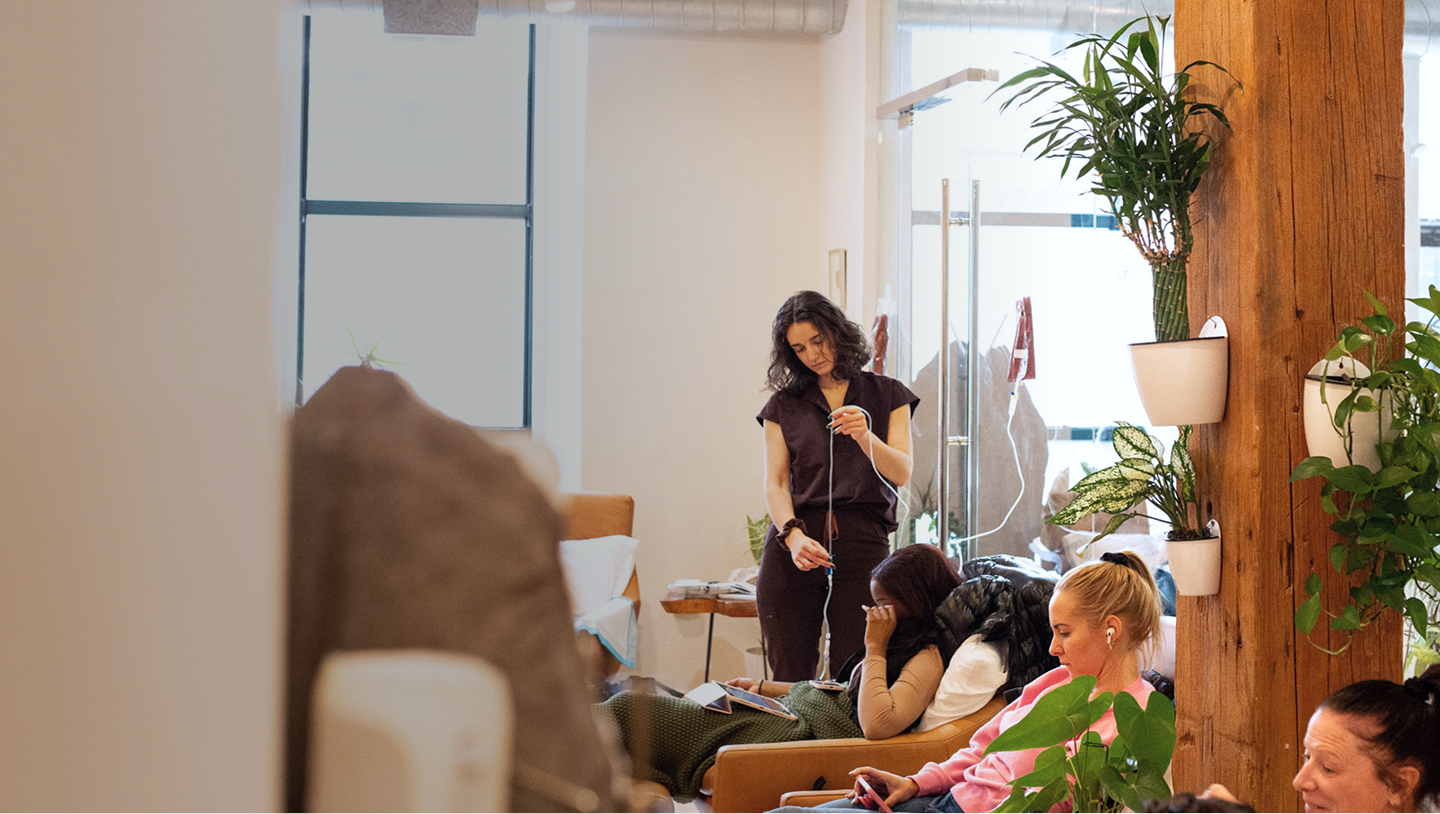 A healthcare professional stands before patients, providing IV therapy in a clinical setting.